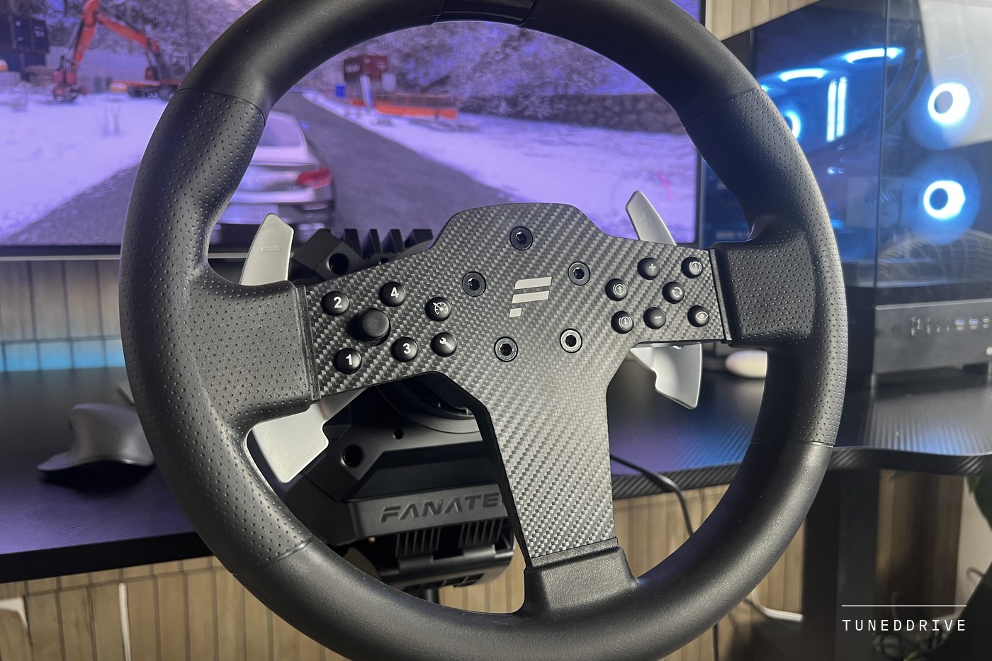 The Fanatec P1 V2 wheel on the CSL DD base in front of a monitor showing a car on a snowy road
