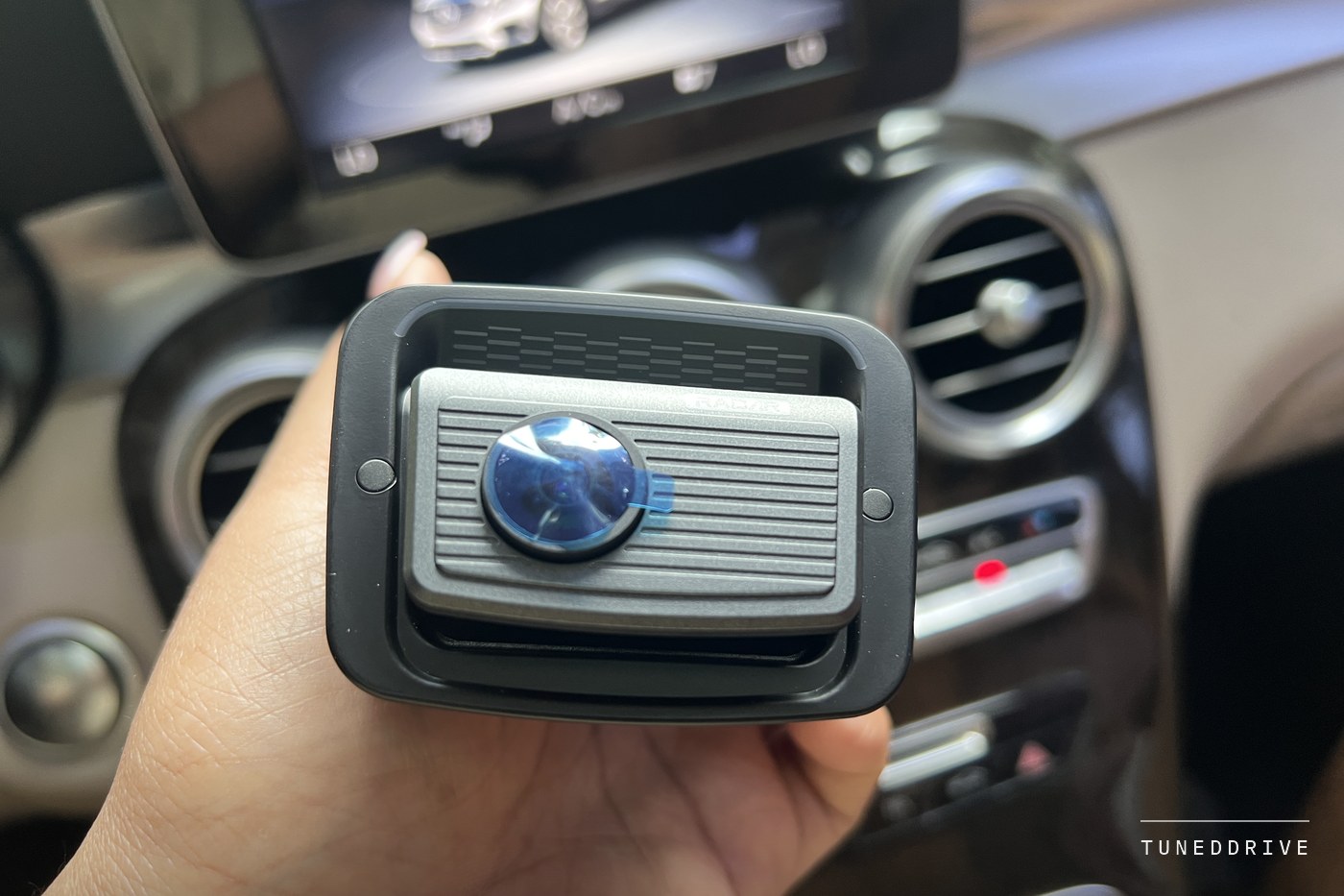 The camera's windshield mount and lens assembly held in one hand in front of the dashboard vents