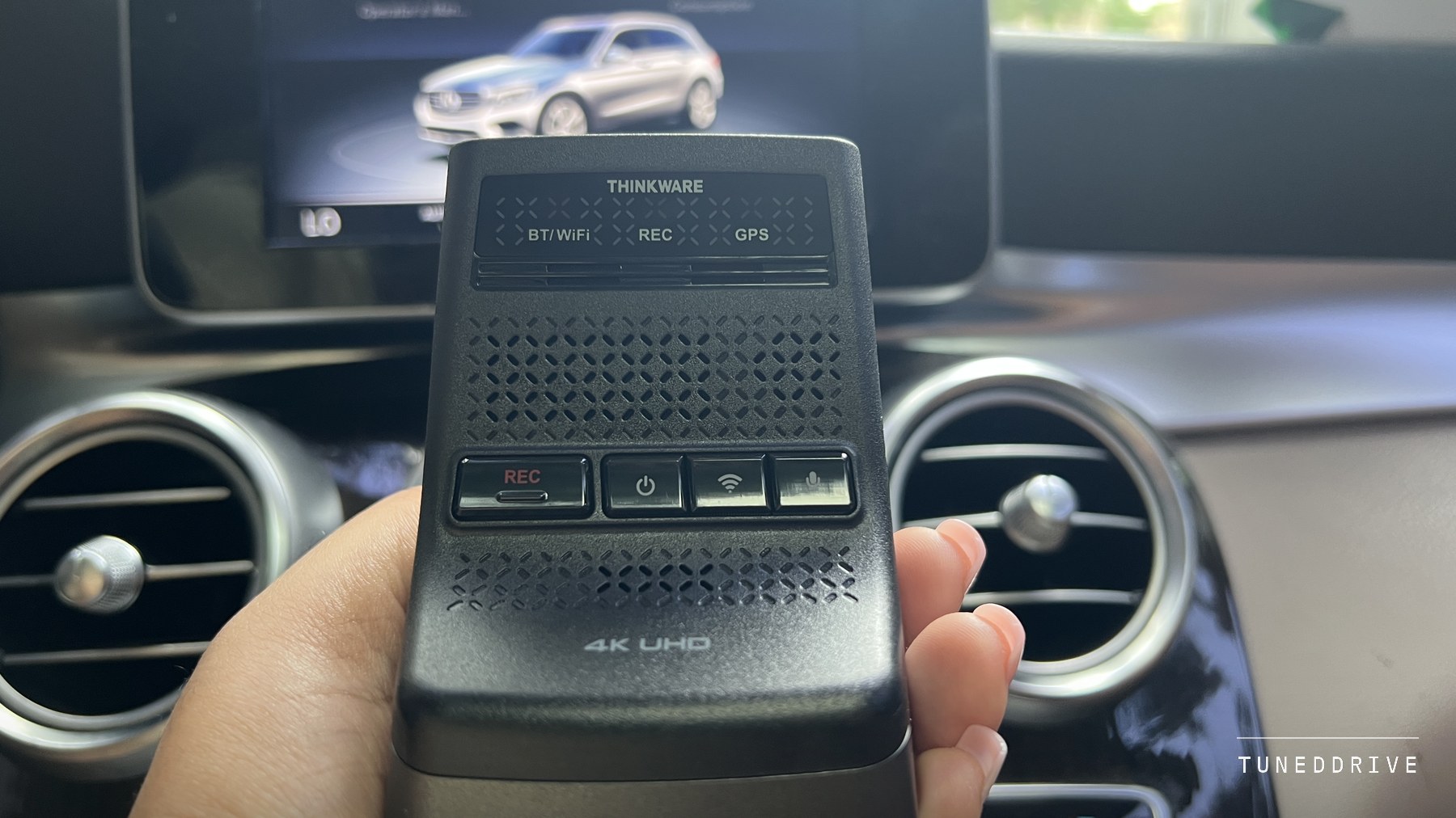 The U3000 PRO front camera held in one hand inside a car, its THINKWARE wordmark and BT, REC and GPS lamps facing the camera, dashboard vents and centre screen behind