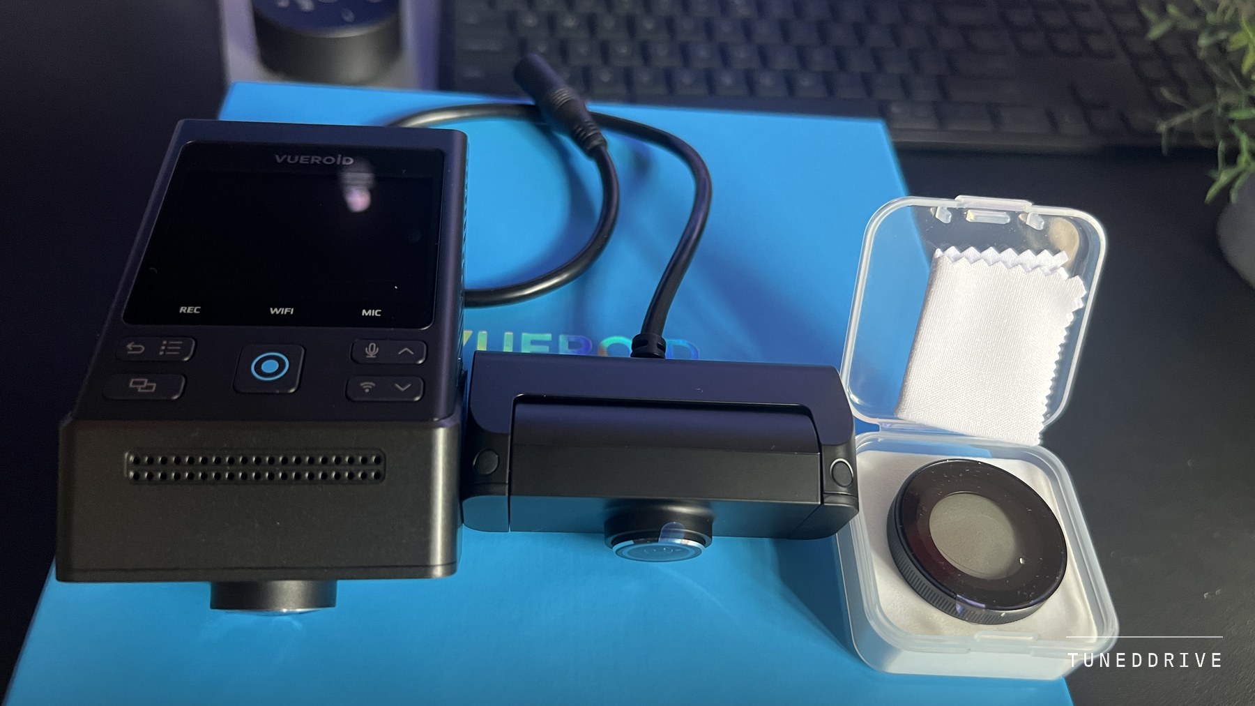 The Vueroid S1 4K Infinite front camera with its screen and buttons, the rear camera on its cable and a CPL filter in a clear case, on the blue Vueroid box