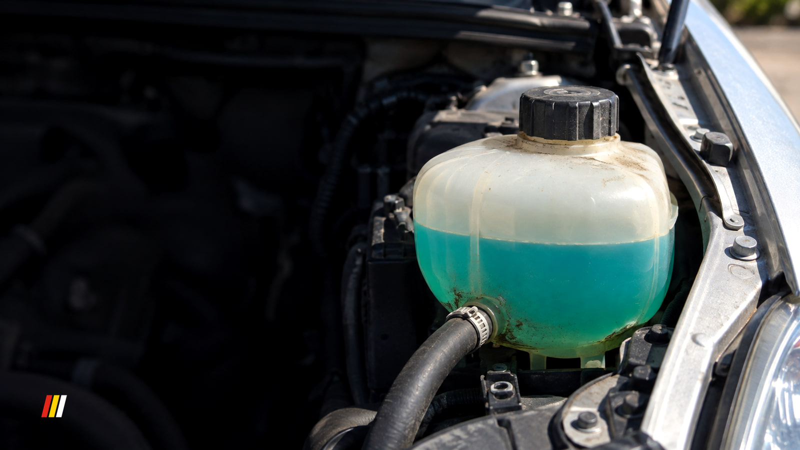 Translucent coolant tank with blue-green antifreeze inside and a black cap, in a silver car's engine bay under hard midday sun.