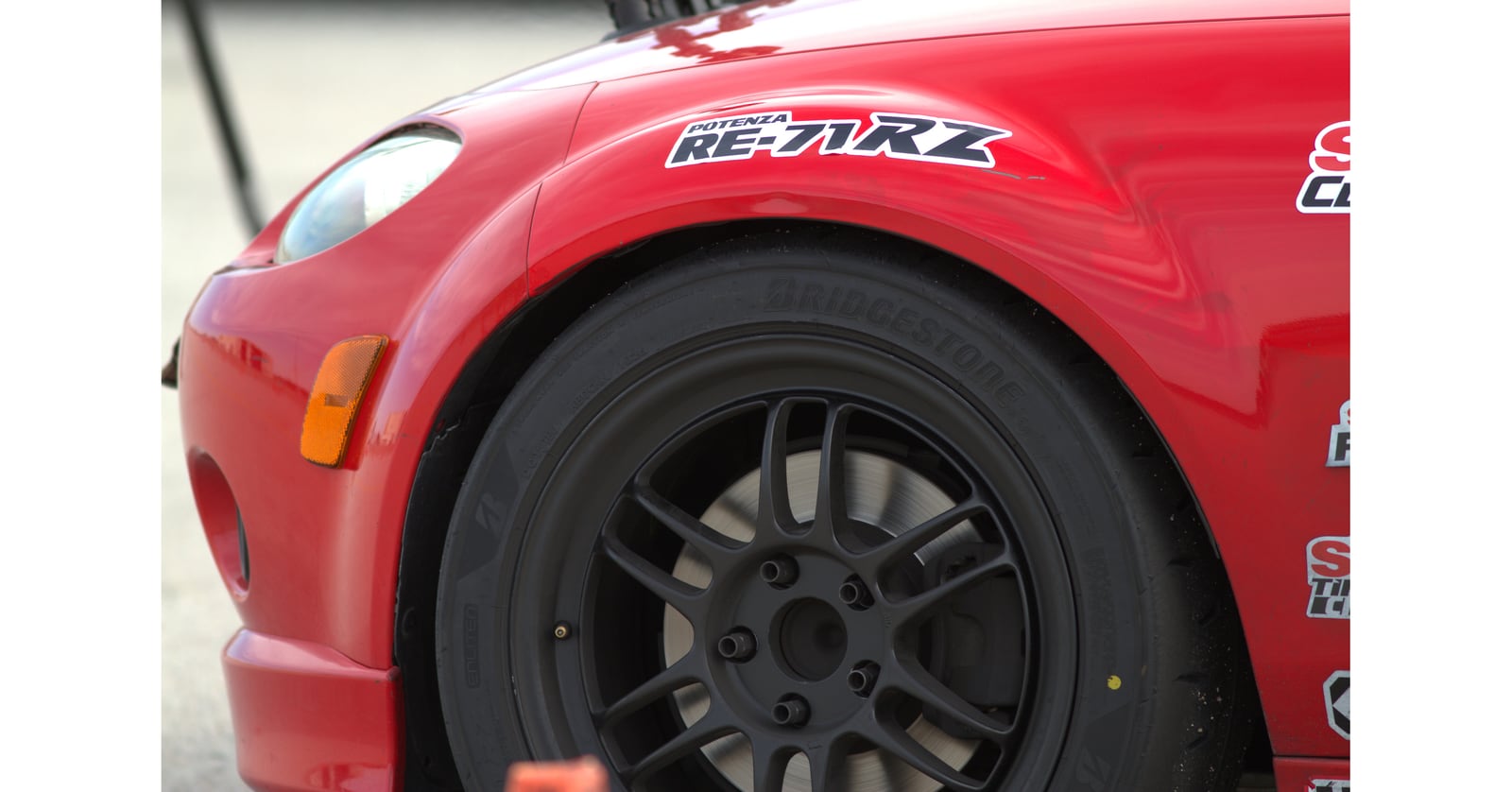 Bridgestone tire on a black wheel beneath a red car fender with a Potenza RE-71RZ decal.