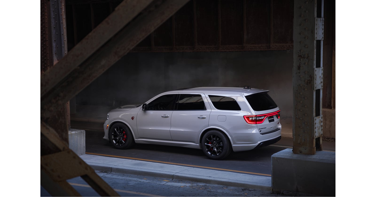 A light grey Dodge Durango with black wheels and red brake calipers parked beneath steel beams.
