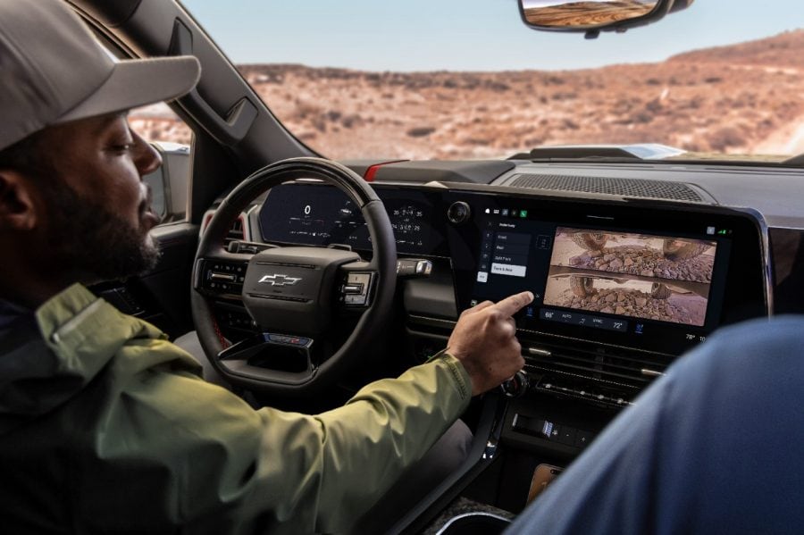 A driver touches a Chevrolet truck's dashboard screen displaying two stacked views of rocky terrain.