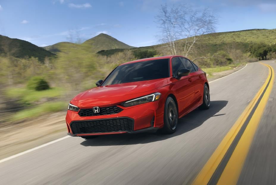 A red Honda Civic driving along a winding road through green hills.