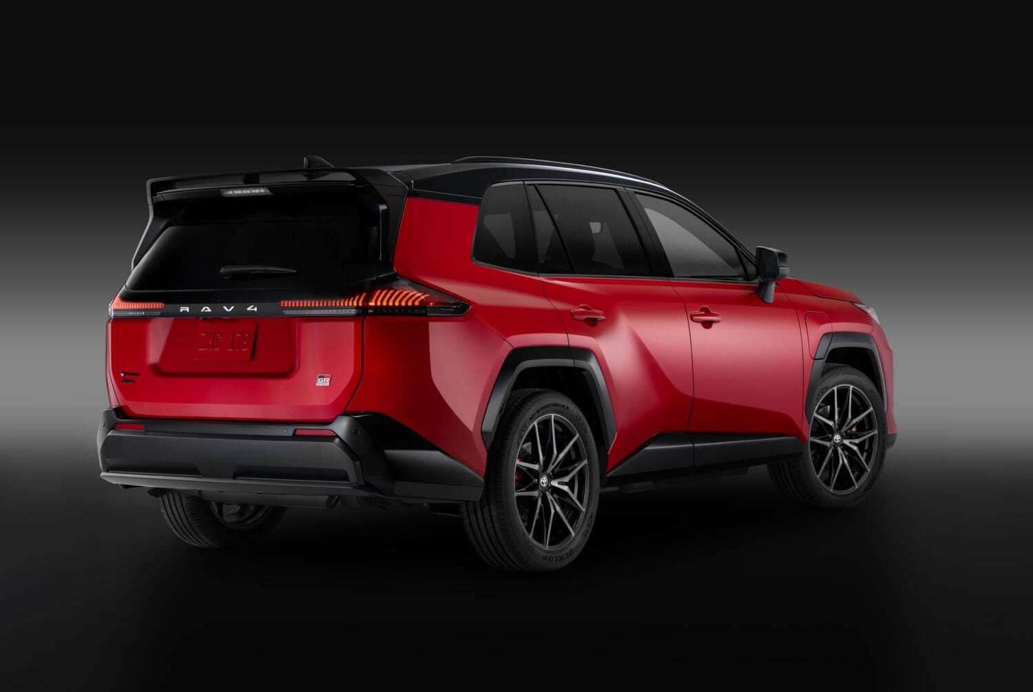 Red Toyota RAV4 Plug-in Hybrid with a black roof, seen from the rear and side.