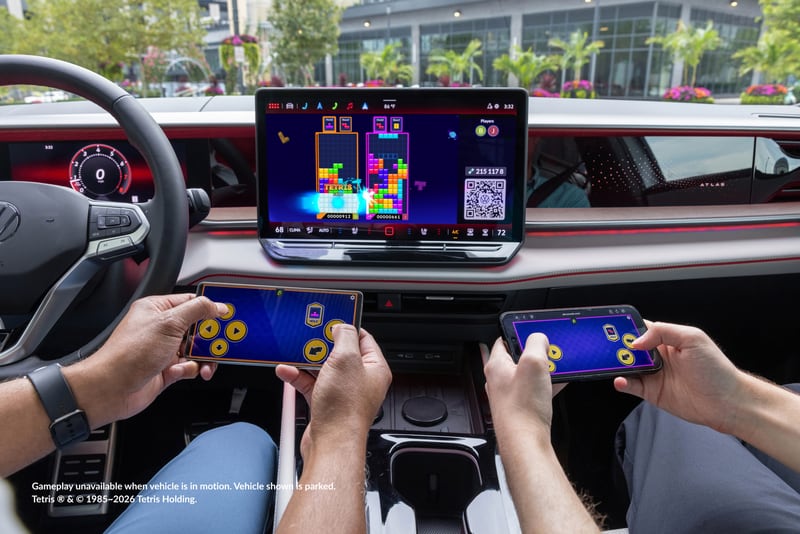 Two occupants hold smartphone controllers while Tetris appears on the vehicle's central display.