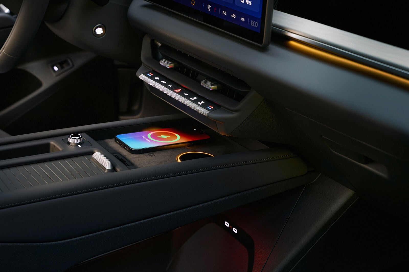 A smartphone charges on the centre console beneath air vents and physical climate buttons.