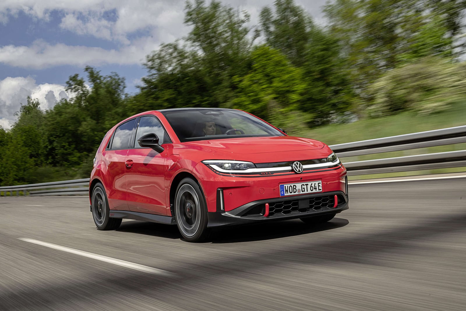 Red Volkswagen ID. Polo GTI driving beside a guardrail, viewed from the front.